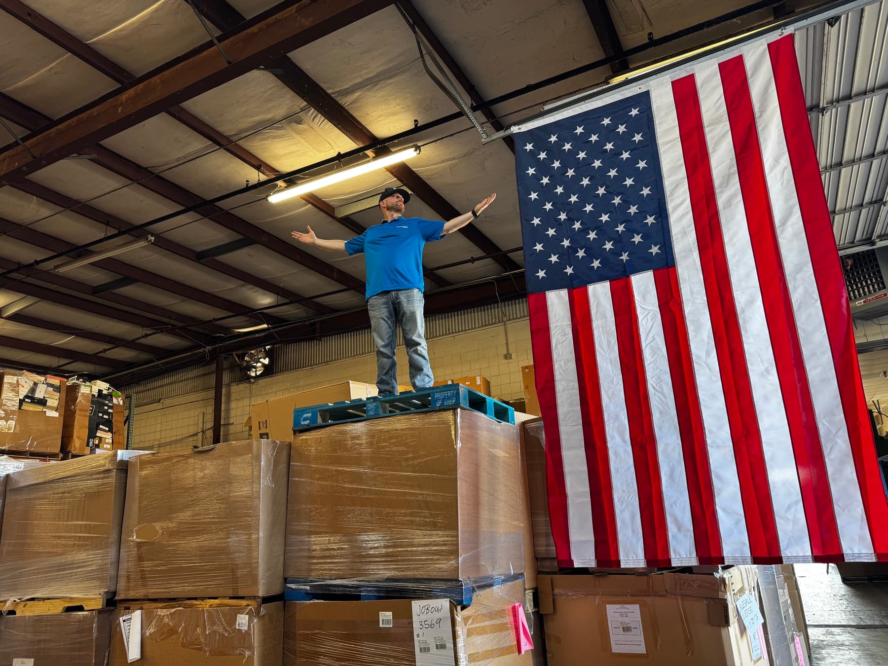 Ryan Nichols standing above pallets in his wholesale warehouse beside a large American flag